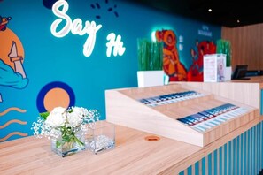 A reception desk with a neon sign, a floral arrangement, and a wall mural. - Kingston Hotel 21 - JO Hotel Johor Bahru (Johor Bahru)