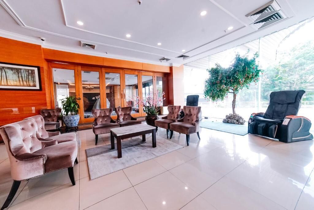 A hotel lobby with seating arrangements, a massage chair, and a large window with a view of trees.
