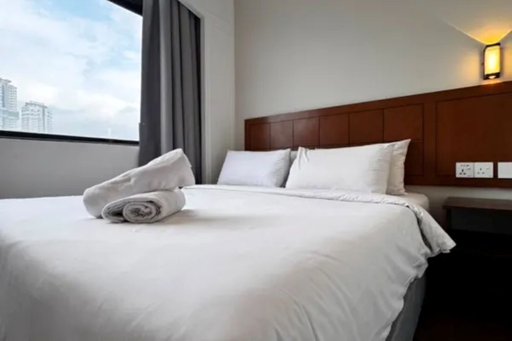 Quarto de hotel com cama bem arrumada, cabeceira e janela com cortinas.