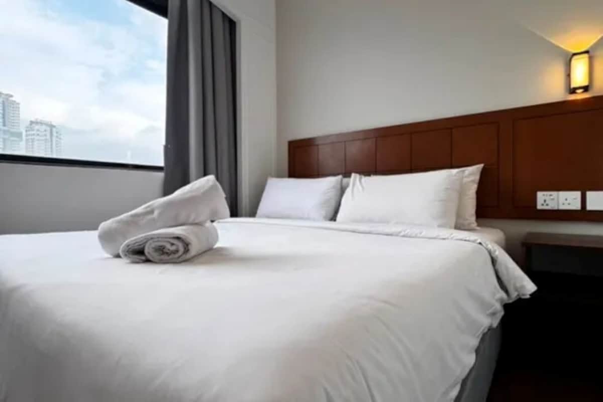 A hotel room with a neatly made bed, a headboard, and a window with curtains.