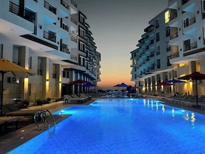 Ein Pool mit Liegestühlen und Sonnenschirmen, umgeben von mehrstöckigen Gebäuden mit Balkonen.