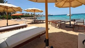 Een terras aan het strand met ligbedden en parasols, met uitzicht op zee.