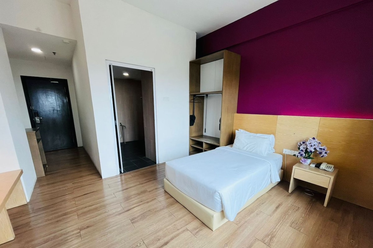 Una habitación de hotel con una cama, mesita de noche y un armario.