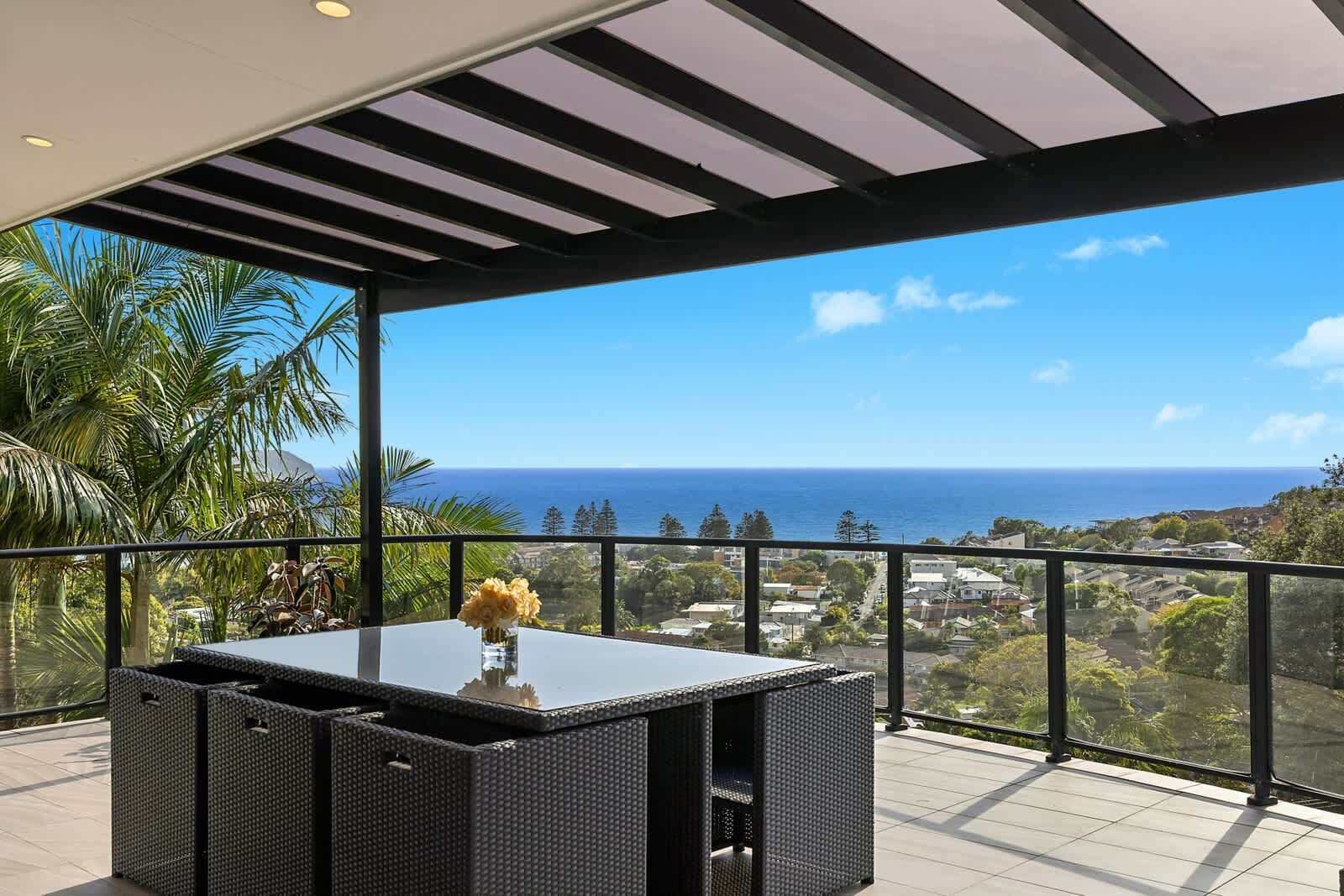 A balcony with a view of the ocean, a table with a vase of flowers, and a pergola structure.