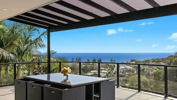 A balcony with a view of the ocean, a table with a vase of flowers, and a pergola structure.