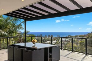 A balcony with a view of the ocean, a table with a vase of flowers, and a pergola structure. - The Outlook by Coast Hosting (Terrigal)