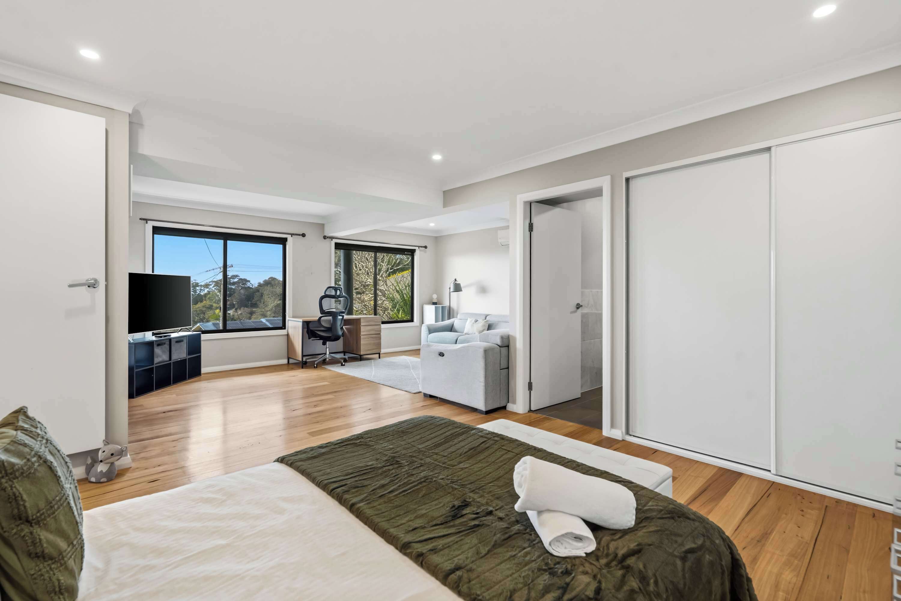 A modern bedroom with a large bed, a desk, and a view of the outdoors.