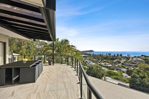 A balcony with a view of a coastal town, a seating area, and a railing. - Terrigal Beach House | 180° Sea View, Private Pool (Terrigal)