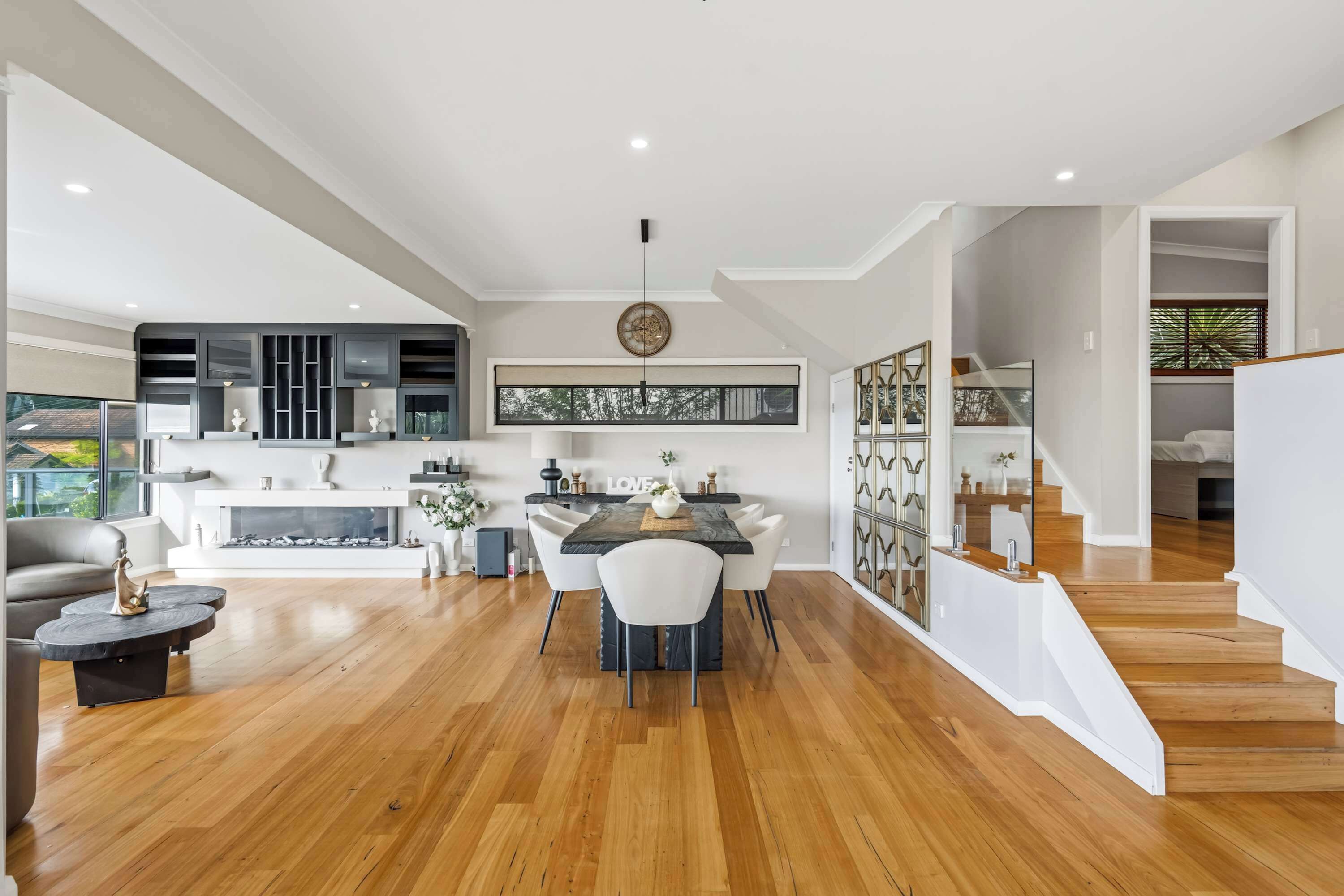 A modern kitchen with a dining area, wooden flooring, and a staircase leading to an upper level.