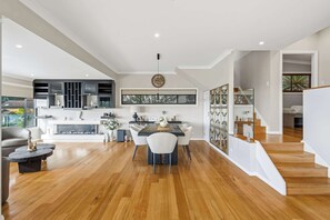A modern kitchen with a dining area, wooden flooring, and a staircase leading to an upper level. - The Outlook by Coast Hosting (Terrigal)