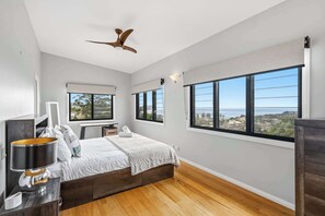 A bedroom with a bed, bedside tables, a lamp, a ceiling fan, and large windows with a view. - Terrigal Beach House | 180° Sea View, Private Pool (Terrigal)