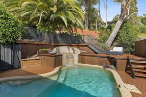 A swimming pool with a waterfall feature, surrounded by wooden decking and a metal fence. - Terrigal Beach House | 180° Sea View, Private Pool (Terrigal)