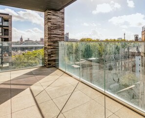 Un balcone con ringhiera in vetro, pavimento piastrellato e vista sulla città.