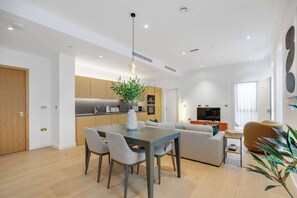 Un soggiorno moderno con zona pranzo, cucina e televisione sullo sfondo.