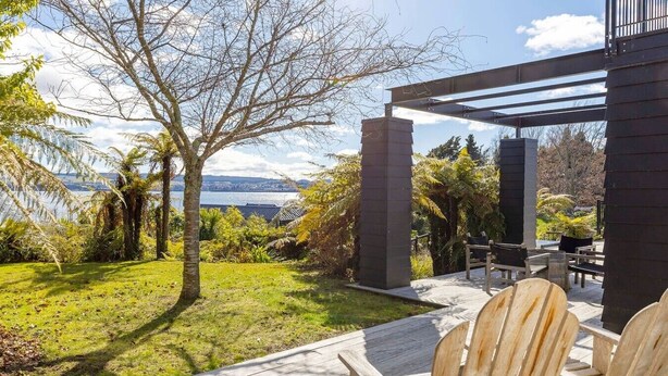 Un patio con sillas de madera, vista al agua y una estructura de edificio moderna.