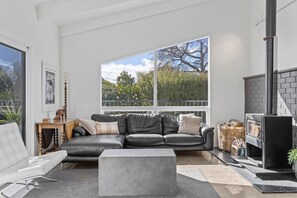 A modern living room with a large window, a fireplace, a sofa, and a coffee table. - Bayview Modern, Stunning views & Hot Tub (Taupō)