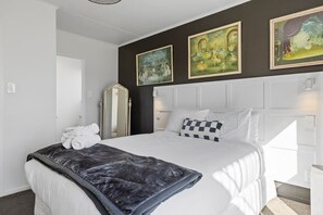 A hotel room with a large bed, a mirror, and three paintings on the wall. - Bayview Modern, Stunning views & Hot Tub (Taupō)