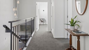Un pasillo con una escalera, una silla, una planta en maceta y un espejo en la pared.