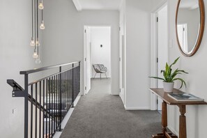Ein Flur mit Treppe, einem Sessel, einer Topfpflanze und einem Spiegel an der Wand.