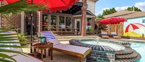 Un espace piscine avec des chaises longues, un jacuzzi et une terrasse équipée de parasols.