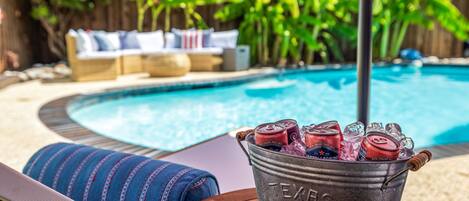 A poolside area with a bucket of canned beverages, a lounge chair, and a pool.