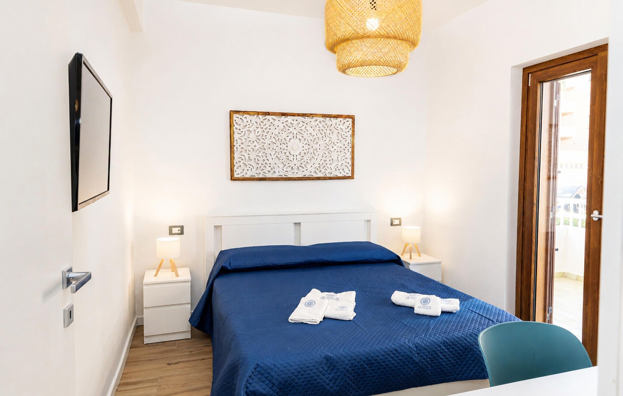 Una camera d'albergo con un letto, lampade sui comodini, un elemento decorativo a parete e una porta che dà su uno spazio all'aperto.