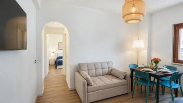 Ett modernt vardagsrum med en soffa, ett matbord, stolar, en lampa och en tv.