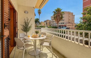 A balcony with a table set for two, chairs, a potted plant, and a view of the street and buildings. - Maison marina Suite - Corfù (Paola)