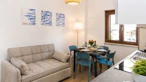 A living room with a sofa, a dining table with chairs, and artwork on the wall. - Maison marina Suite - Corfù (Paola)