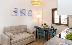 A living room with a sofa, a dining table with chairs, and artwork on the wall. - Maison marina Suite - Corfù (Paola)