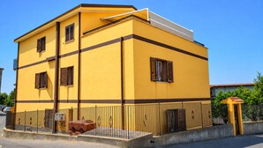 A two-story building with a yellow facade, multiple windows with shutters, and a metal fence in front. - 1 bedroom gorgeous apartment in Saline Joniche (Saline Joniche)