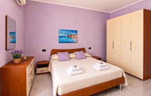 Ein Schlafzimmer mit einem Bett, einem Kleiderschrank, einem Nachttisch, einer Lampe und einem Bild an der Wand.