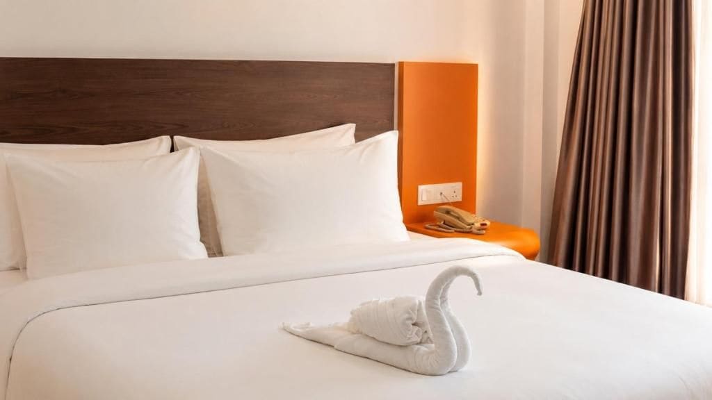 A hotel room with a neatly made bed, a headboard, a nightstand with a telephone, and a swan-shaped towel.