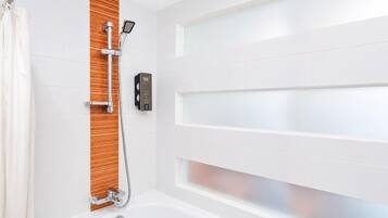 Un baño con ducha, panel de control y pared de azulejos blancos.