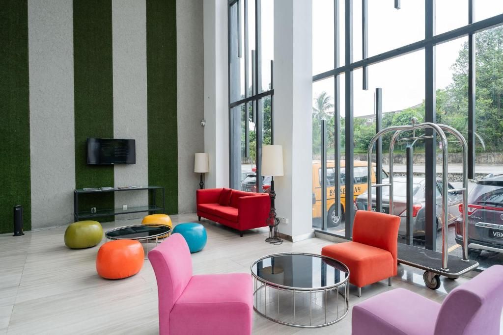 A modern lobby with a glass wall, a red sofa, colorful chairs, and a television on the wall.