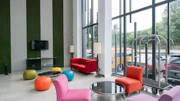 A modern lobby with a glass wall, a red sofa, colorful chairs, and a television on the wall.