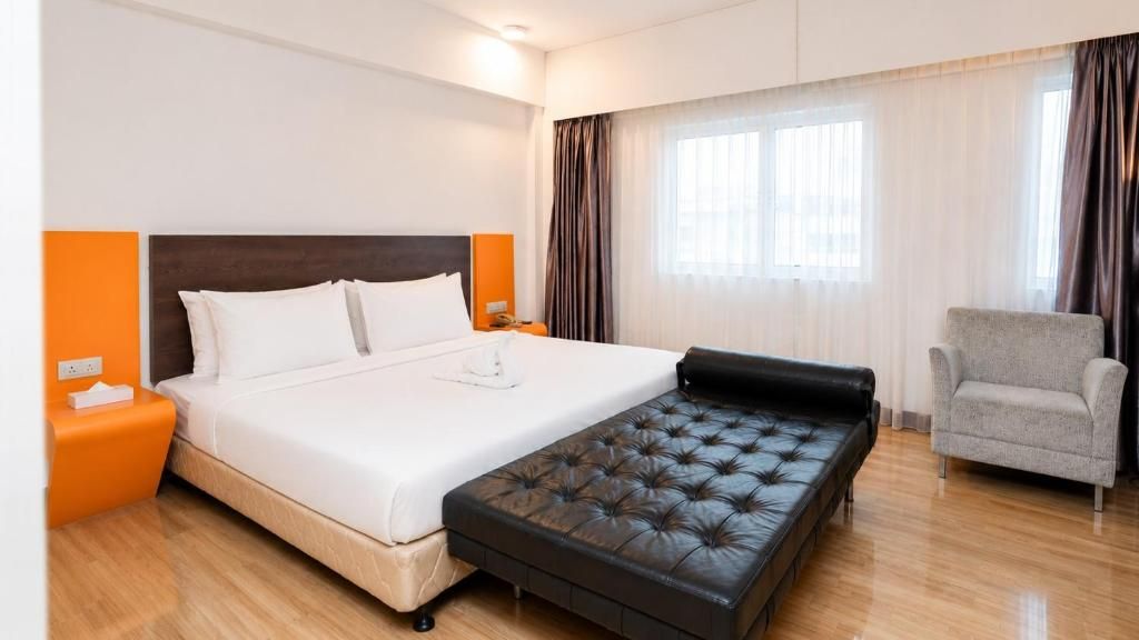 Habitación de hotel con cama, sofá, sillón y ventana con cortinas.