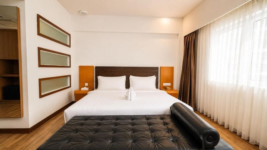 A hotel room with a large bed, bedside tables, a wardrobe, and a window with curtains.