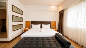 Una habitación de hotel con una cama grande, mesitas de noche, un armario y una ventana con cortinas.