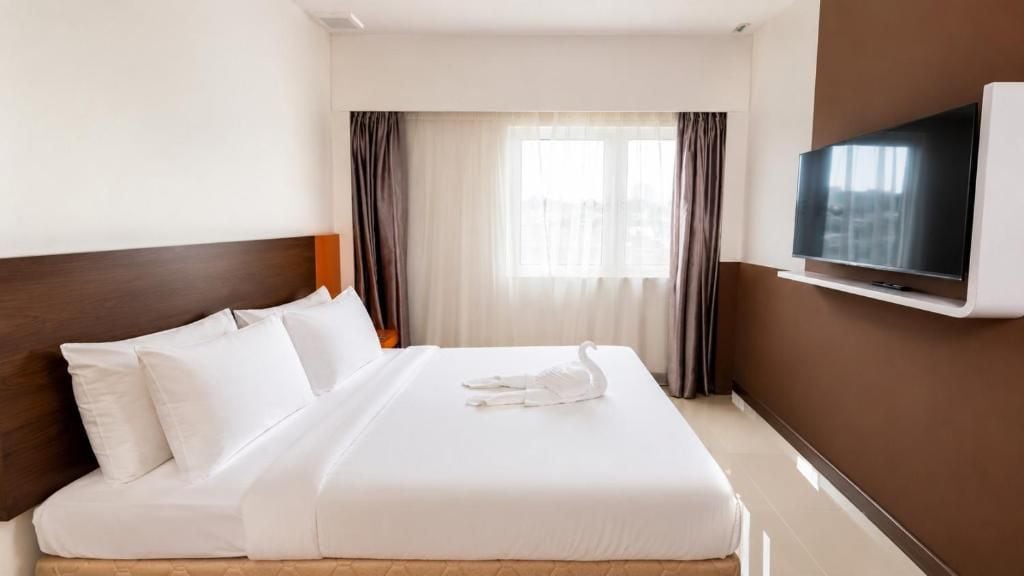Una habitación de hotel con una cama, un televisor montado en la pared y una ventana con cortinas.
