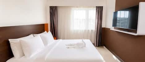 A hotel room with a bed, a television mounted on the wall, and a window with curtains.