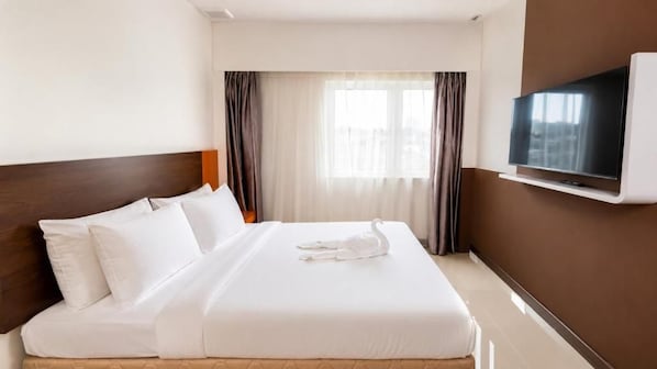 A hotel room with a bed, a television mounted on the wall, and a window with curtains.