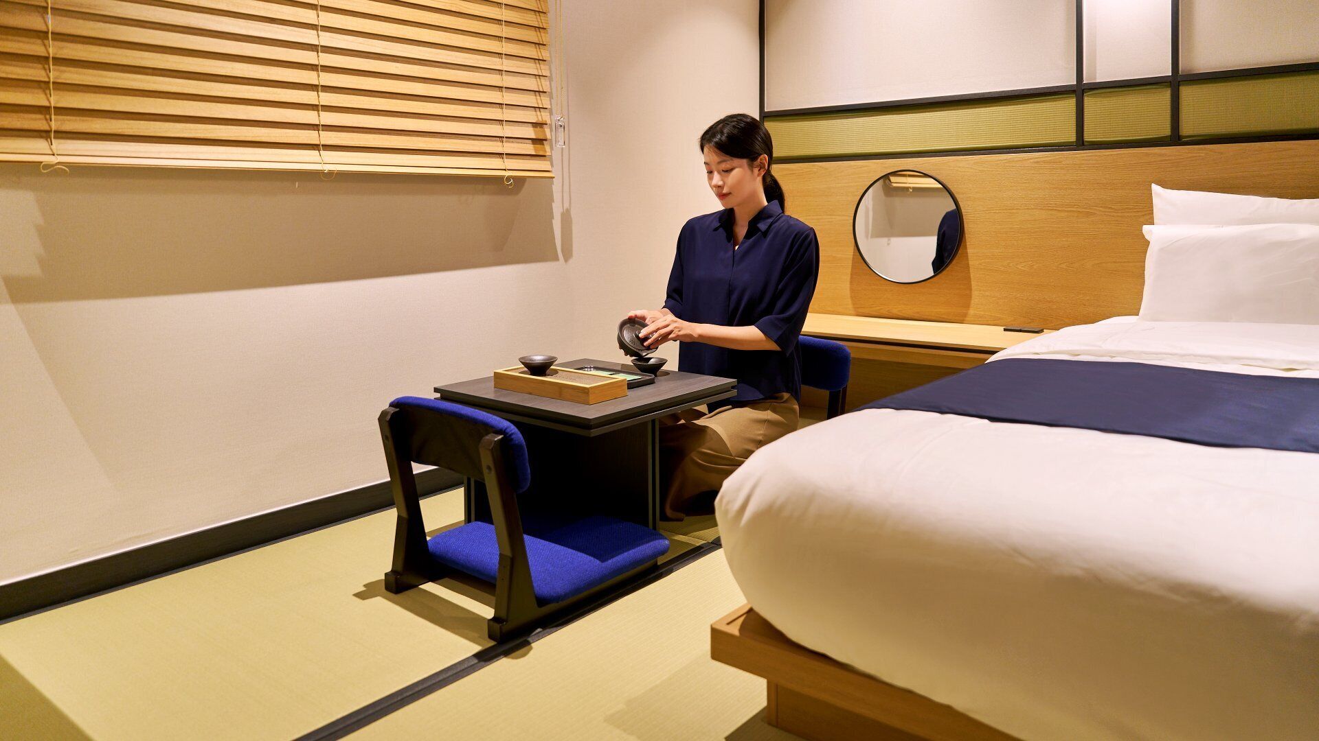 Hotelkamer met een bed, een klein tafeltje met theeservies, een stoel en een houten hoofdeinde met spiegel.