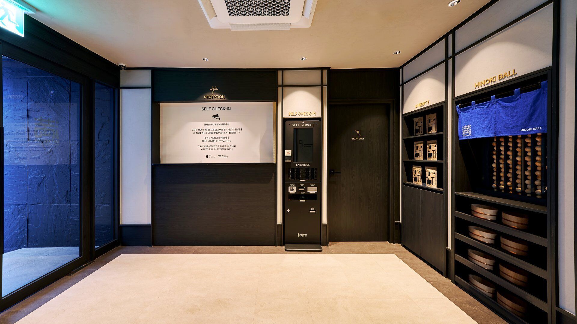Zona de recepción de un hotel con un quiosco de auto-registro, un mostrador de recepción y una exhibición de cuencos de madera.