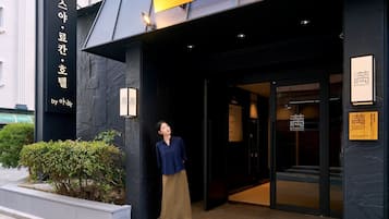 A hotel entrance with a dark facade, a person standing at the doorway, and bilingual signage.