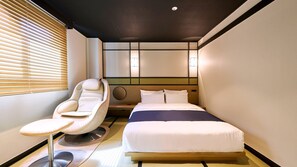 A hotel room with a bed, a massage chair, and a window with blinds.