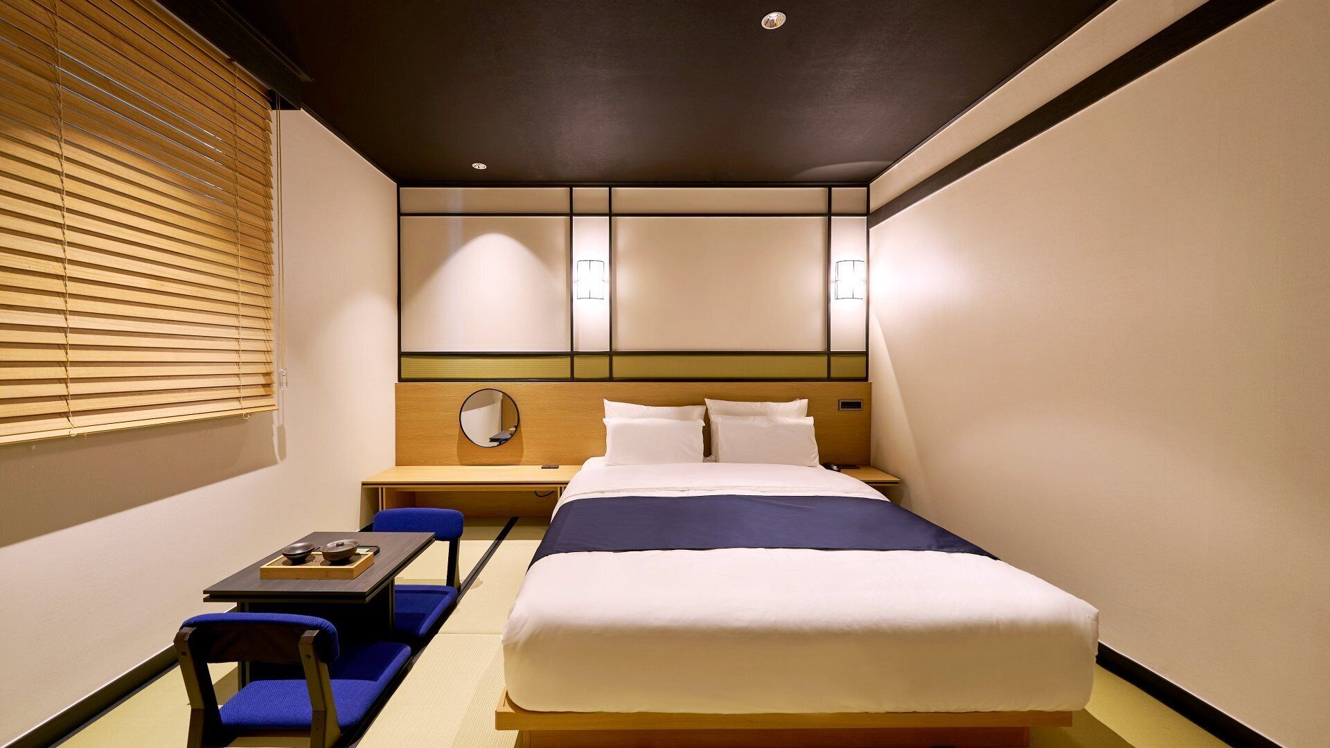 Habitación de hotel con cama, escritorio, silla y una pequeña mesa con un bol y una taza.