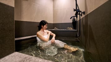 Una persona en un jacuzzi pequeño y cerrado, con un grifo y una botella de jabón.