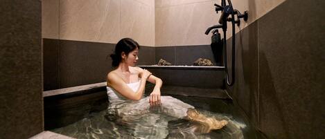 Una persona en un jacuzzi pequeño y cerrado, con un grifo y una botella de jabón.