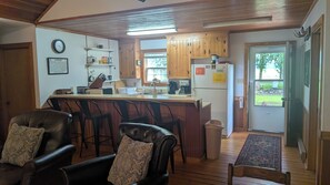 A compact kitchen with wooden cabinets, a bar area with leather chairs, and a view of the outdoors through a door.